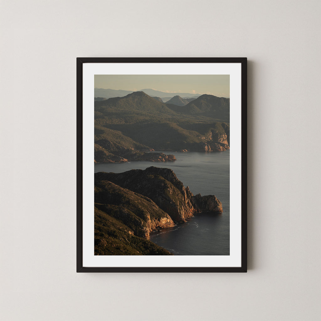 Freycinet art print showing an aerial view of the Tasmanian coastline and ocean at sunrise, displayed on a wall in a black frame.