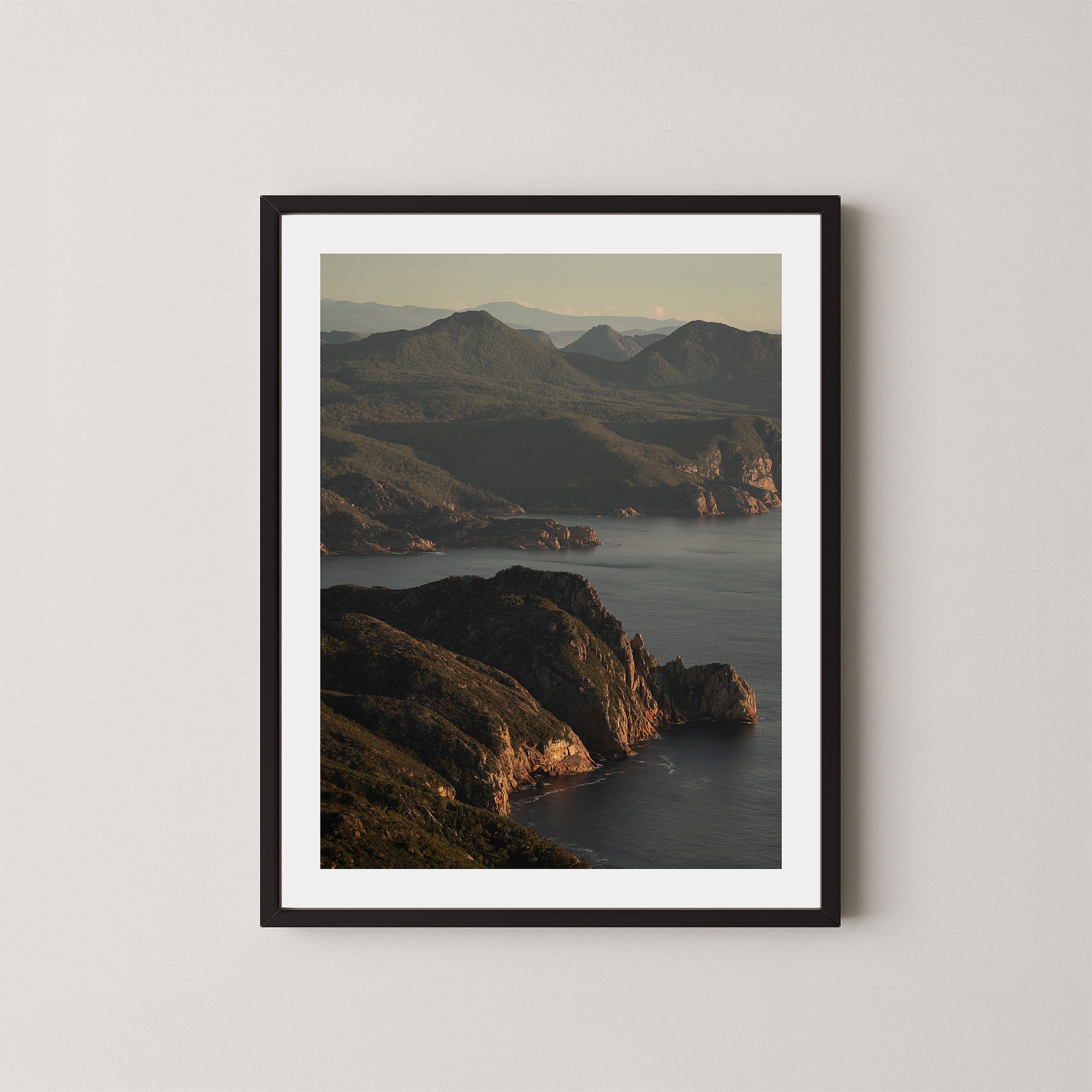 Freycinet art print showing an aerial view of the Tasmanian coastline and ocean at sunrise, displayed on a wall in a black frame.