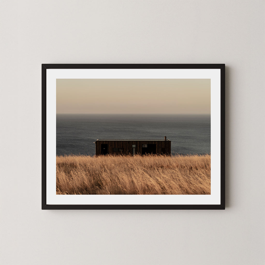 Haven art print of a serene coastal scene with a small building and ocean on Kangaroo Island, Australia, shown in a black frame on a wall.  