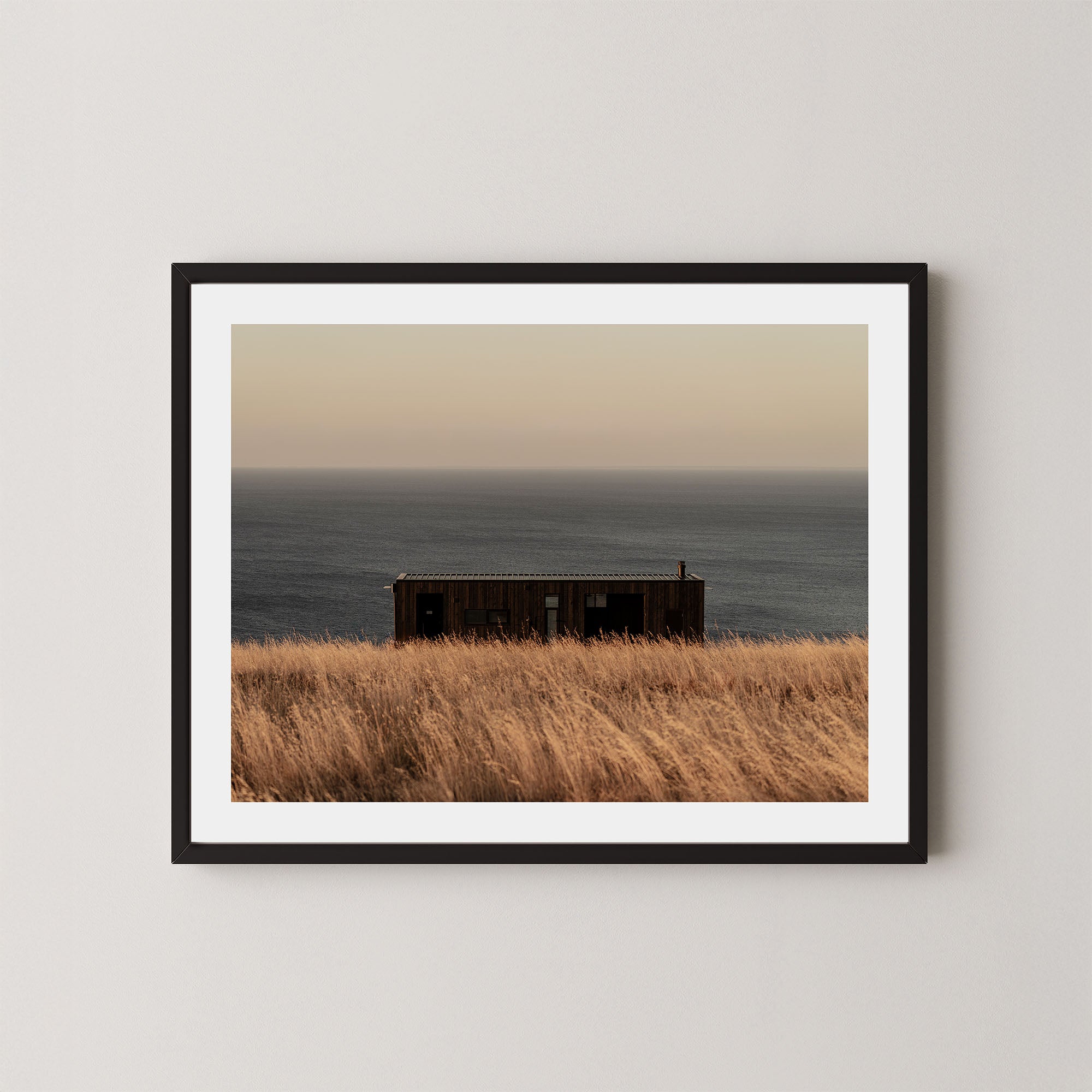 Haven art print of a serene coastal scene with a small building and ocean on Kangaroo Island, Australia, shown in a black frame on a wall.  