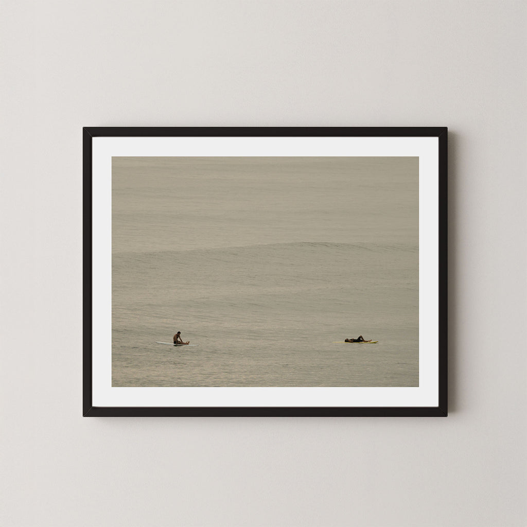Ocean Therapy art print of two surfers on a calm ocean at Byron Bay, Australia, displayed on a wall in black frame.
