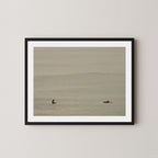 Ocean Therapy art print of two surfers on a calm ocean at Byron Bay, Australia, displayed on a wall in black frame.