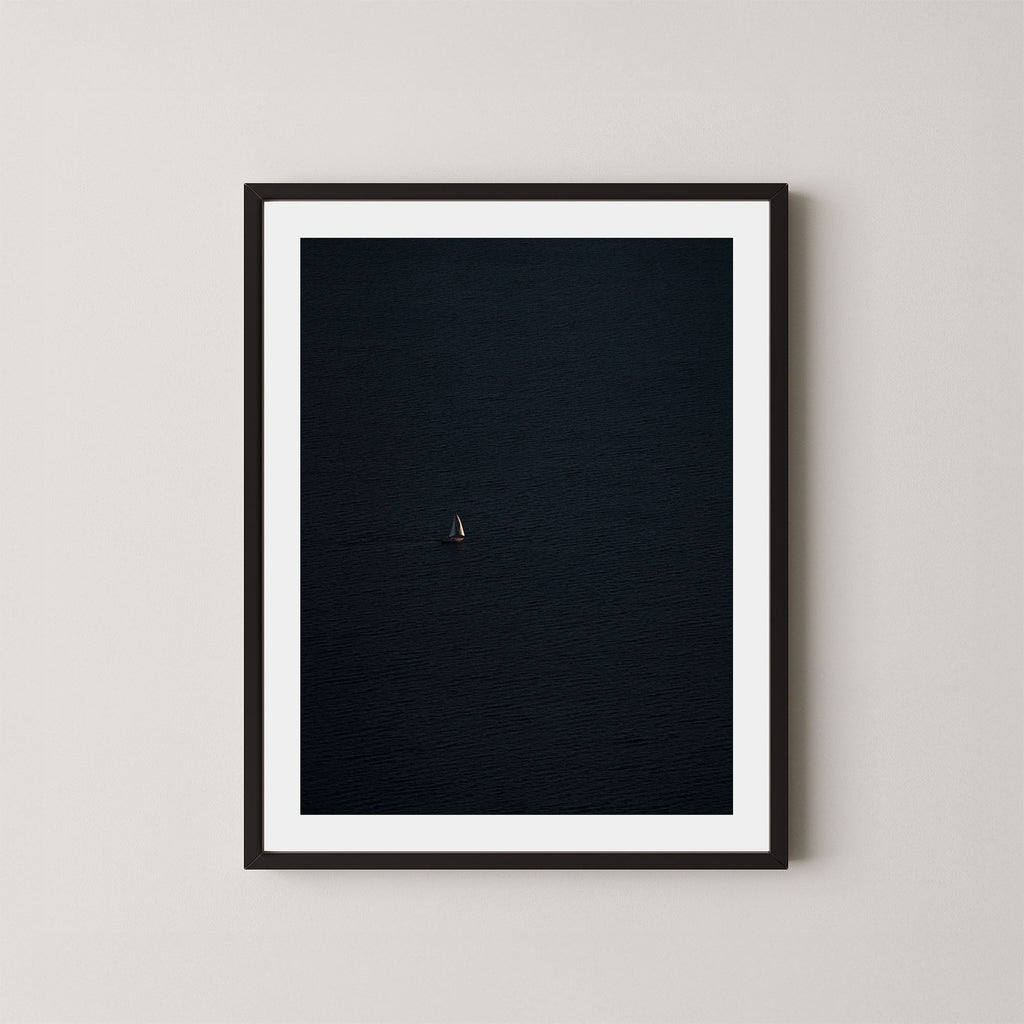 Voyage art print featuring a single sailing boat on the ocean, displayed on a wall in a black frame.