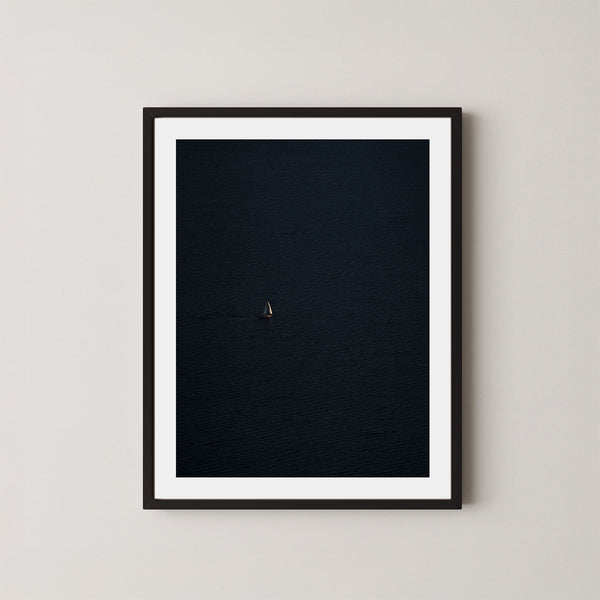 Voyage art print featuring a single sailing boat on the ocean, displayed on a wall in a black frame.