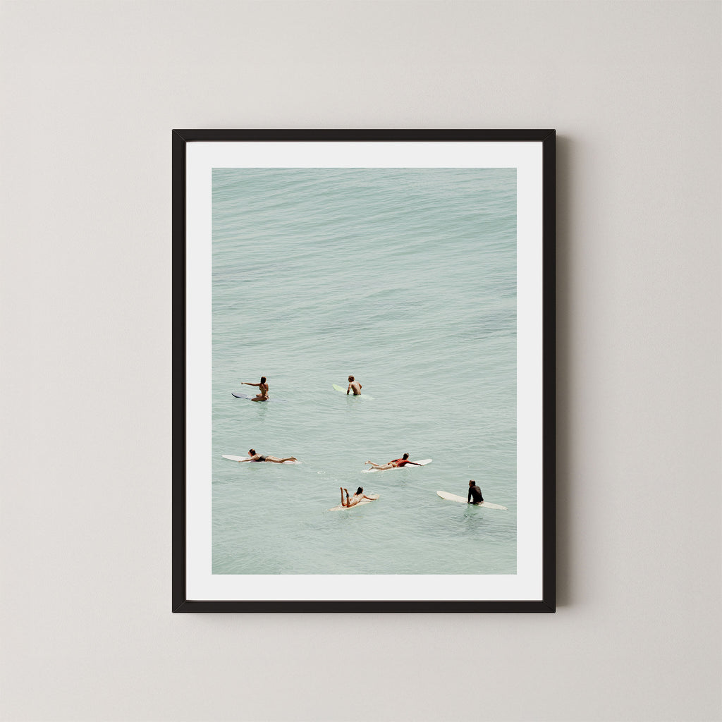 Fine photography artwork of people on surfboards in the water, displayed in a black frame. 