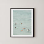 Fine photography artwork of people on surfboards in the water, displayed in a black frame. 