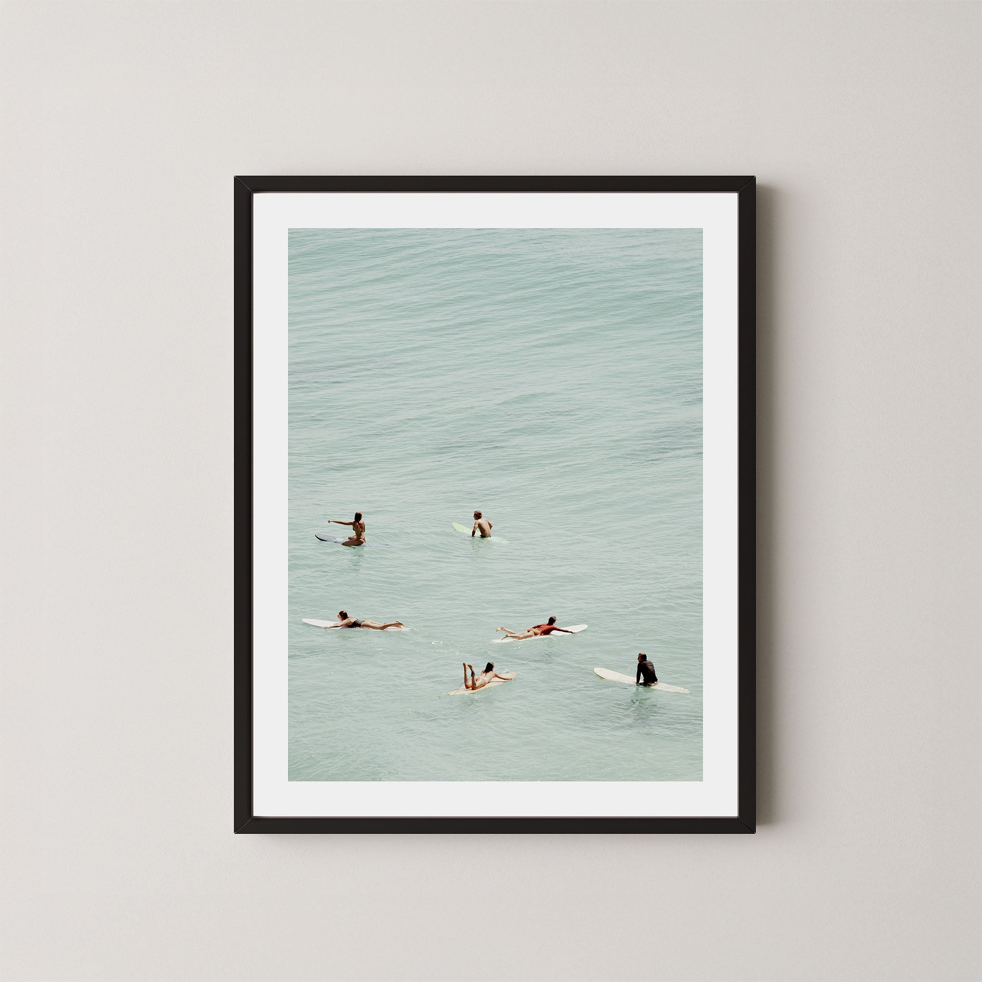 Fine photography artwork of people on surfboards in the water, displayed in a black frame. 