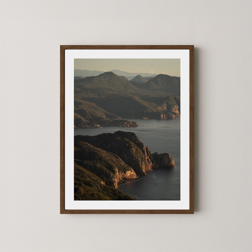 Freycinet art print showing an aerial view of the Tasmanian coastline and ocean at sunrise, displayed on a wall in a dark wooden frame.