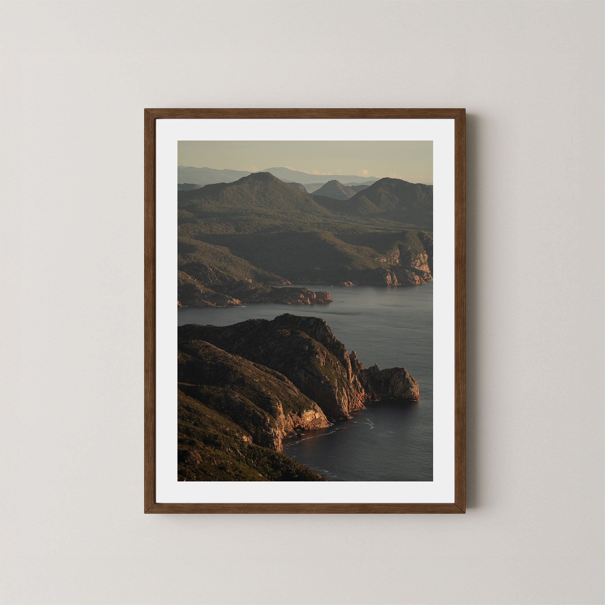 Freycinet art print showing an aerial view of the Tasmanian coastline and ocean at sunrise, displayed on a wall in a dark wooden frame.