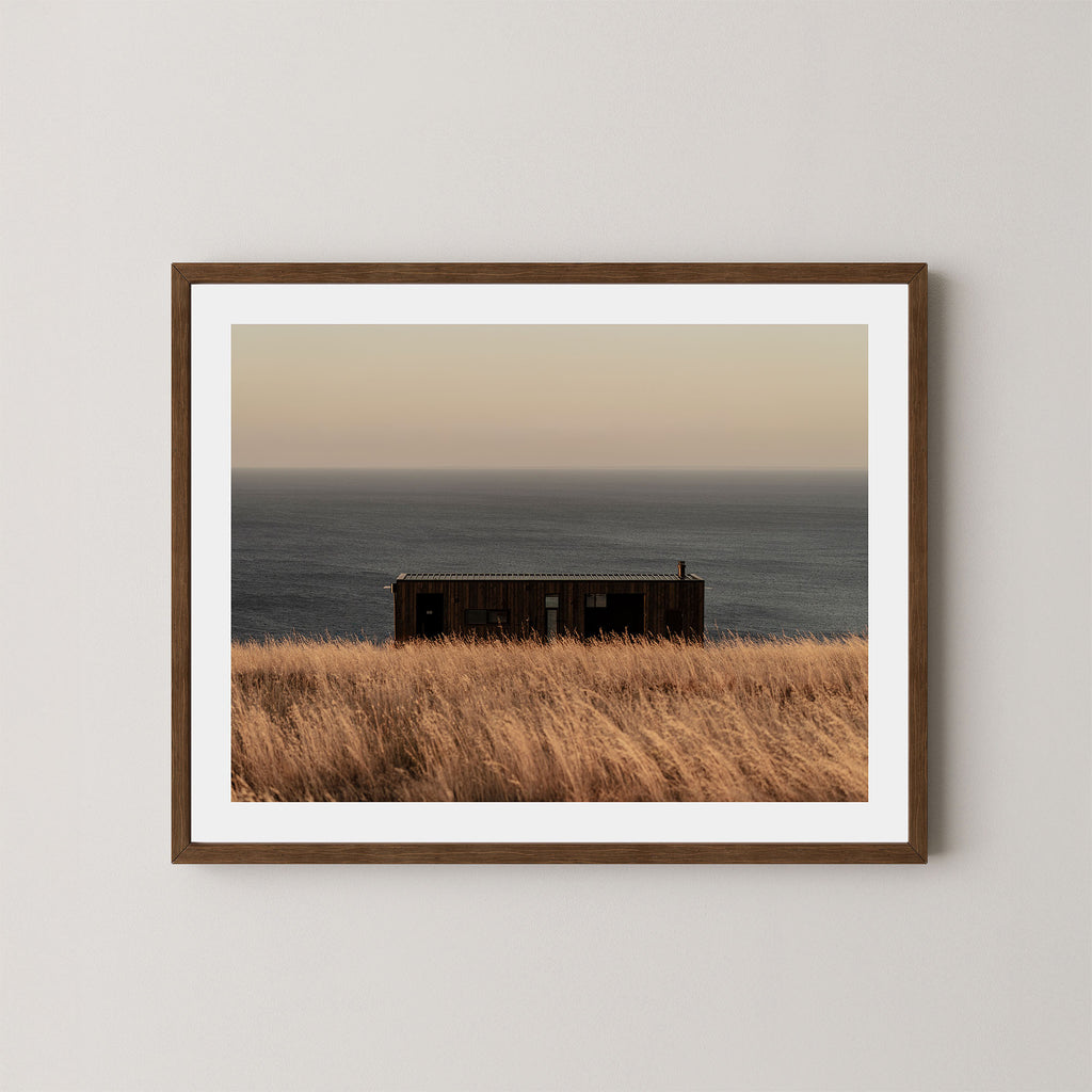 Haven art print of a serene coastal scene with a small building and ocean on Kangaroo Island, Australia, displayed on a wall in a dark wooden frame.