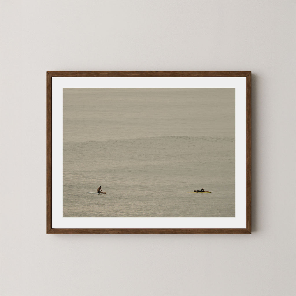 Ocean Therapy art print of two surfers on a calm ocean at Byron Bay, Australia, displayed on a wall in dark wooden frame.