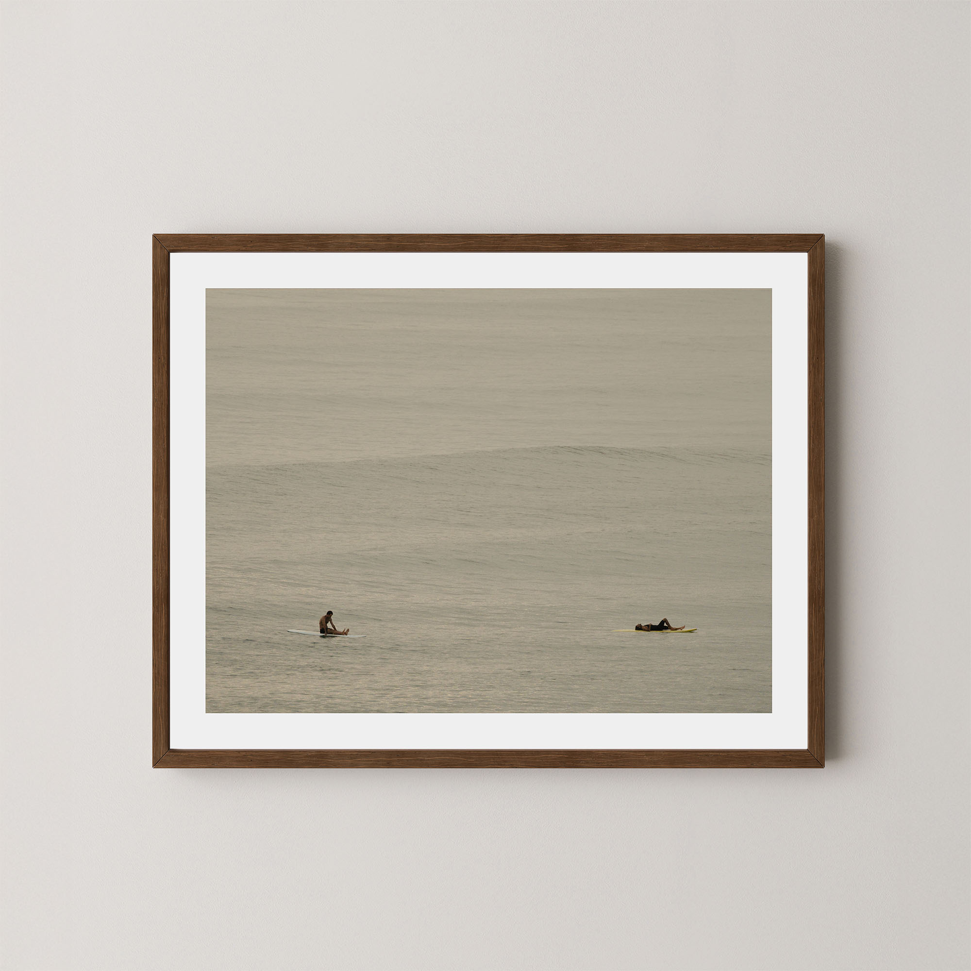 Ocean Therapy art print of two surfers on a calm ocean at Byron Bay, Australia, displayed on a wall in dark wooden frame.