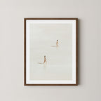 Beach Crossing art print featuring two women walking in opposite directions on a light, sandy beach at low tide in Byron Bay, Australia, displayed on a wall in a dark wooden frame.