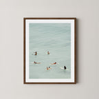 Fine photography artwork of people on surfboards in the water, displayed in a dark wooden frame. 