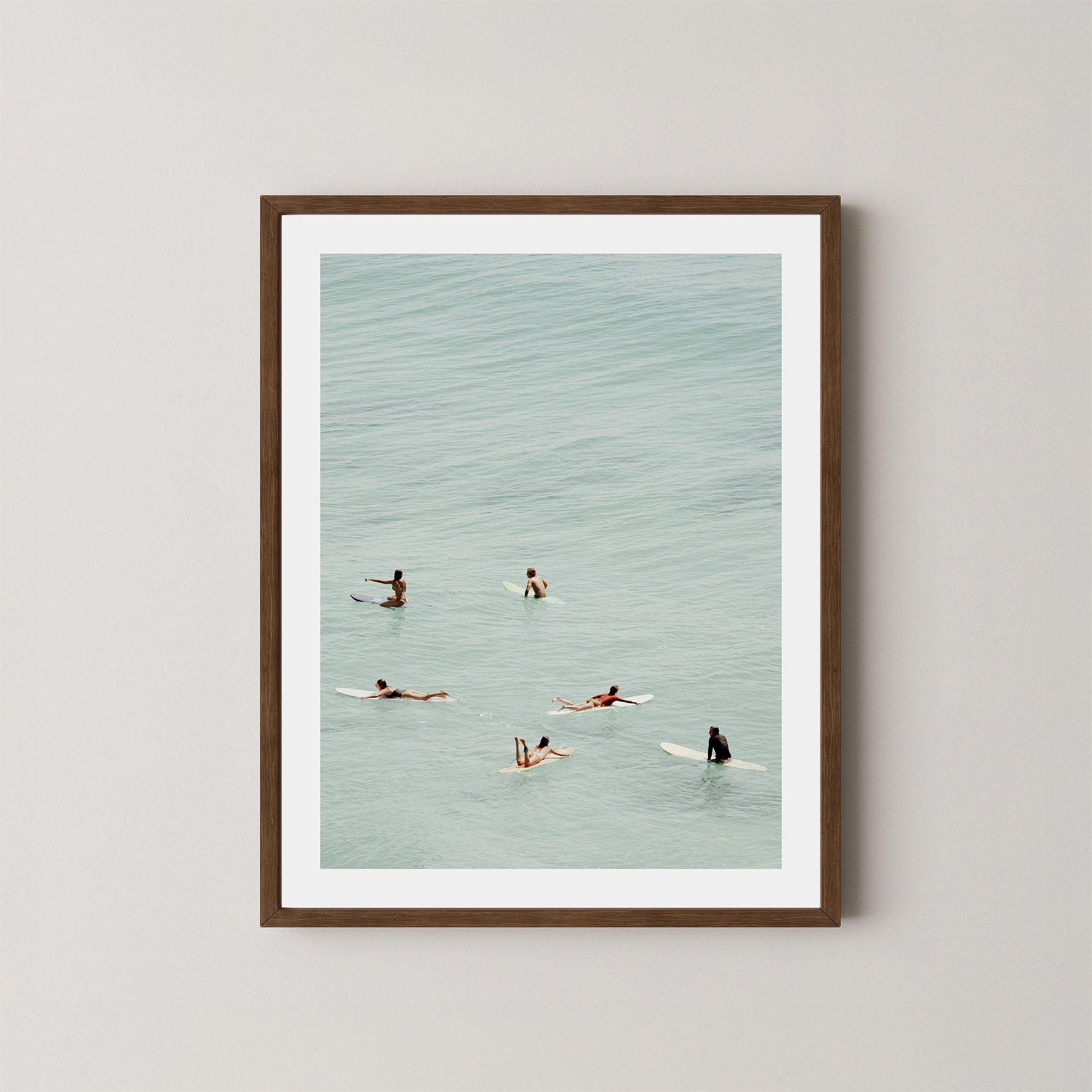 Fine photography artwork of people on surfboards in the water, displayed in a dark wooden frame. 