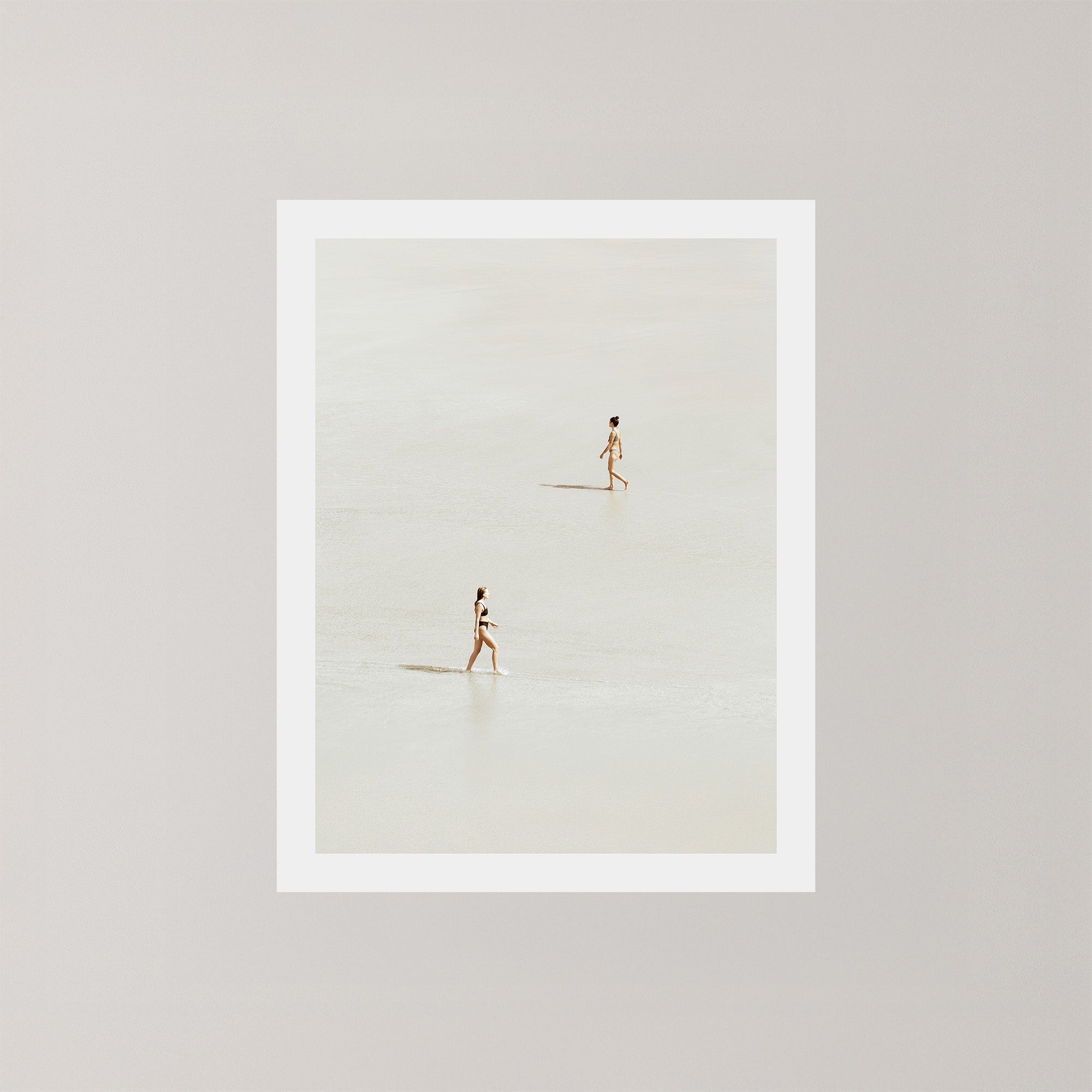 Beach Crossing photography art print featuring two women walking in opposite directions on a light, sandy beach at low tide in Byron Bay, Australia.