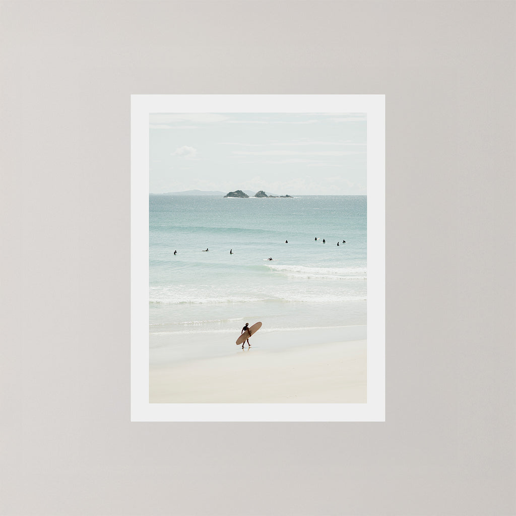 Wategos Calm photo art print of a surfer walking with a surfboard on the beach in Byron Bay, Australia, with the ocean and other surfers in the background.