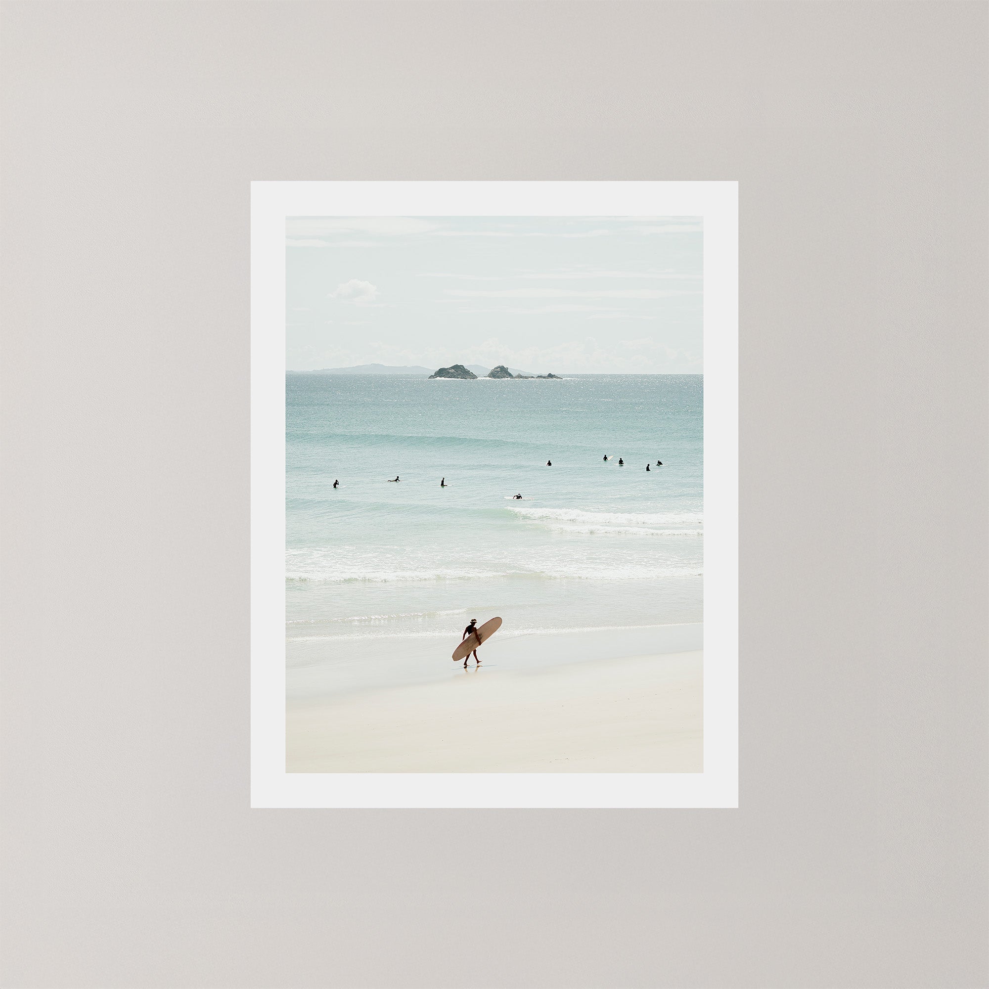 Wategos Calm photo art print of a surfer walking with a surfboard on the beach in Byron Bay, Australia, with the ocean and other surfers in the background.