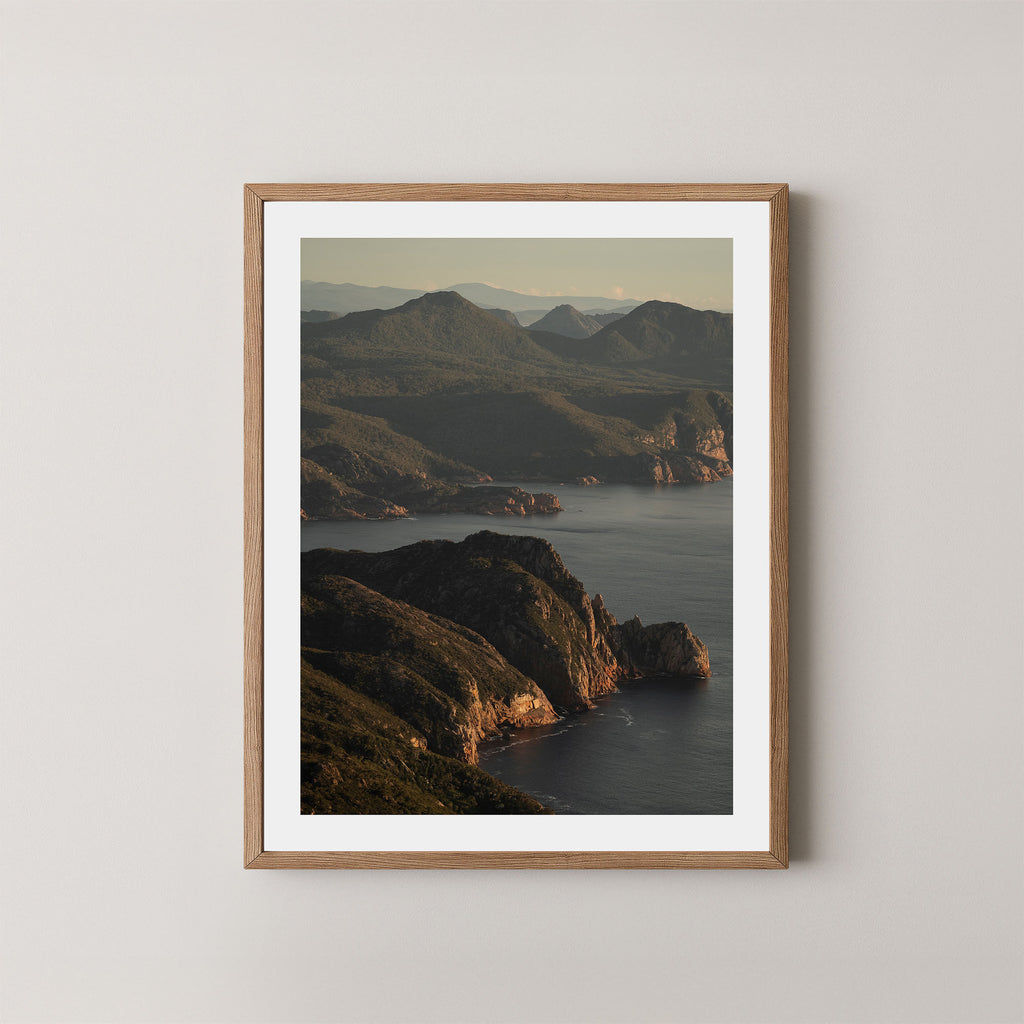 Freycinet art print showing an aerial view of the Tasmanian coastline and ocean at sunrise, displayed on a wall in a natural wooden frame.