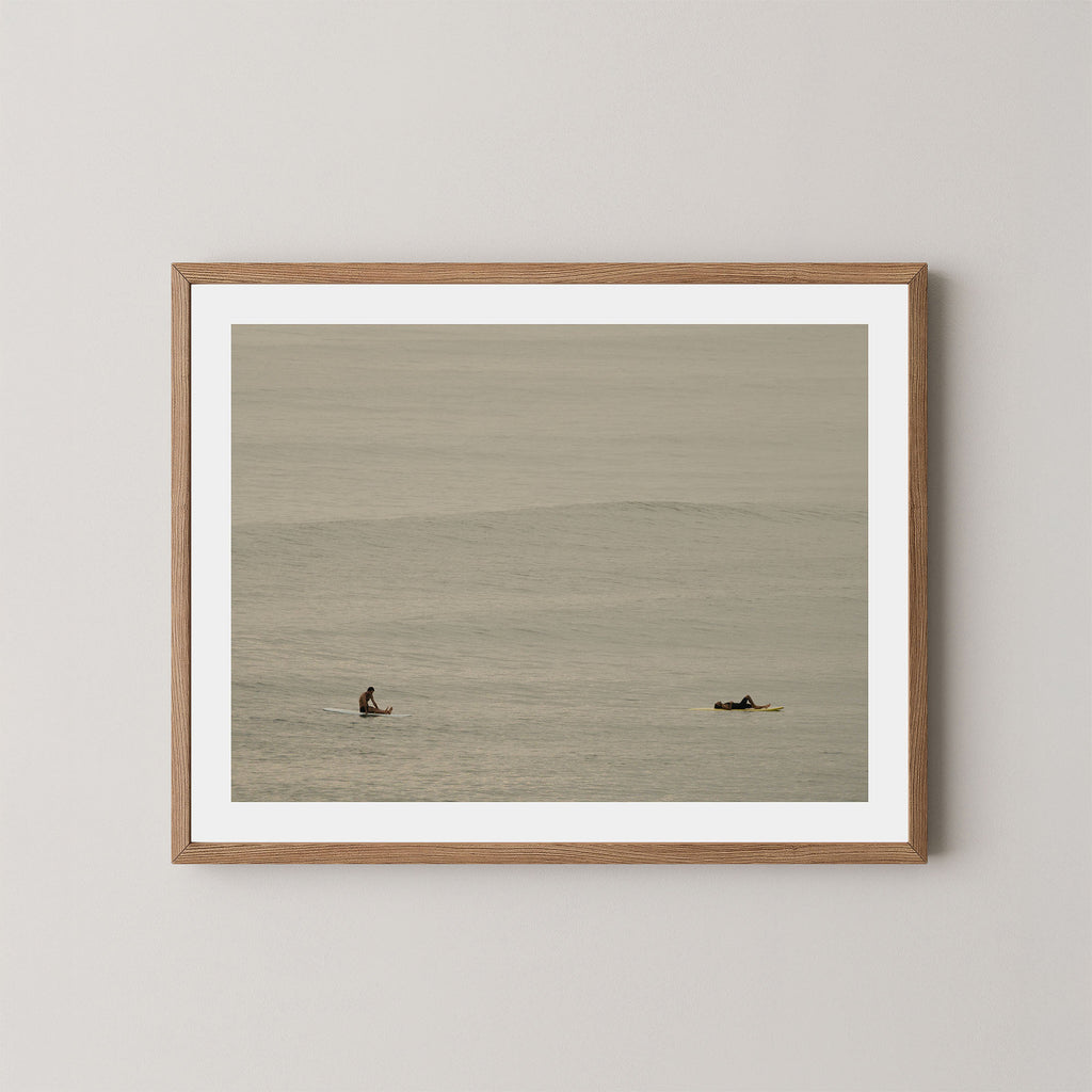 Ocean Therapy art print of two surfers on a calm ocean at Byron Bay, Australia, displayed on a wall in natural wooden frame.