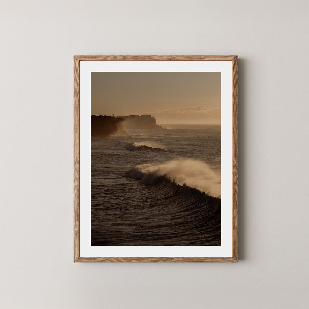 Wave Appreciation art print of Bronte, Sydney with waves and cliffs displayed on a plain wall in a natural oak frame.