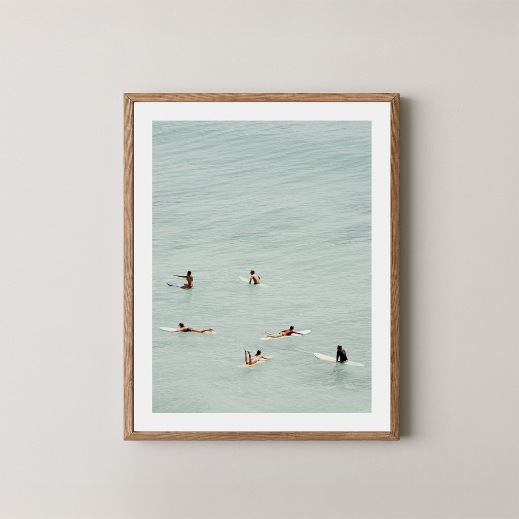 Fine photography artwork of people on surfboards in the water, displayed in a natural wooden frame. 