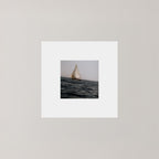 A square art print featuring a small sailboat on dark water under a pale sky, centered within a wide white mat on a light gray background.