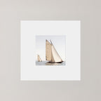 A square art print featuring a photograph of two sailboats on calm water under a pale sky, surrounded by a wide white mat on a light gray background.