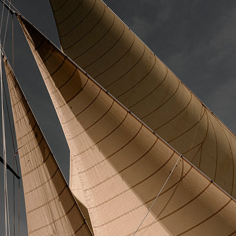 Close-up low-angle view of large beige canvas sails on a sailing vessel against a dark stormy gray sky.