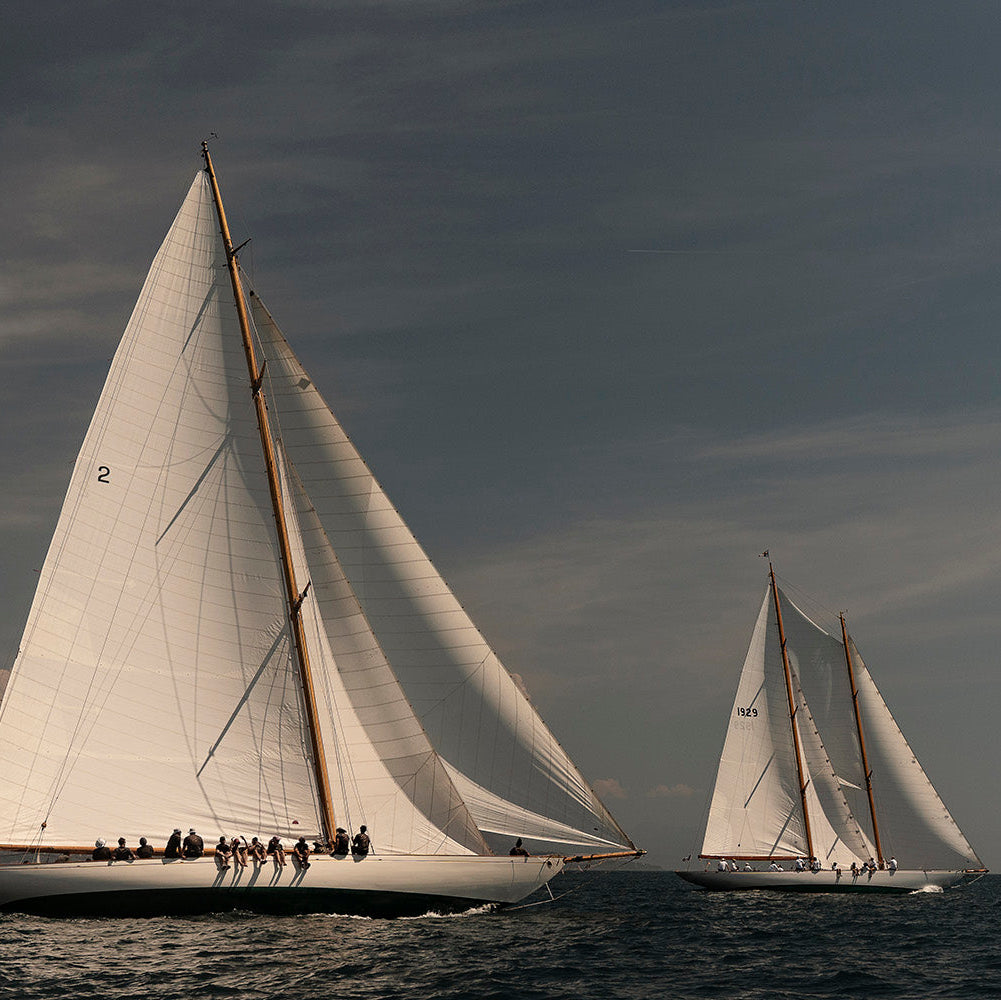 Three white-sailed sailboats racing on the open sea under a dramatic, cloudy sky.