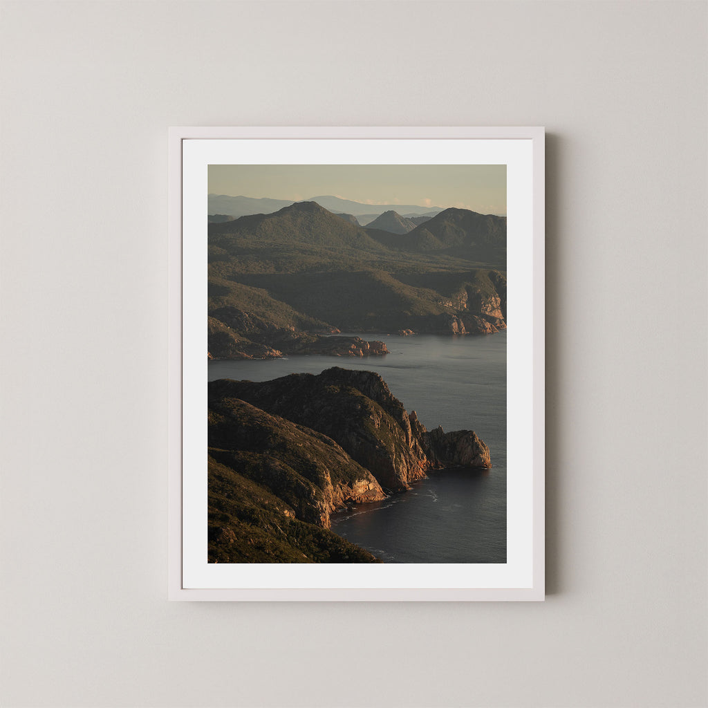 Freycinet art print showing an aerial view of the Tasmanian coastline and ocean at sunrise, displayed on a wall in a white frame.