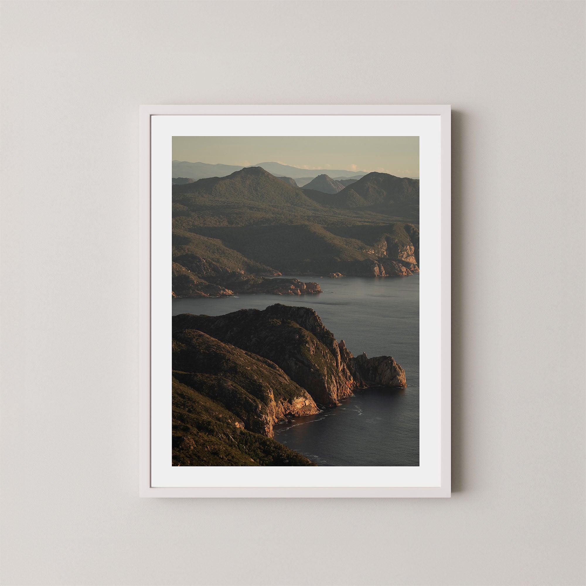 Freycinet art print showing an aerial view of the Tasmanian coastline and ocean at sunrise, displayed on a wall in a white frame.