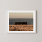 Haven art print of a serene coastal scene with a small building and ocean on Kangaroo Island, Australia, displayed on a wall in a white frame.