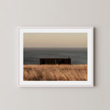 Haven art print of a serene coastal scene with a small building and ocean on Kangaroo Island, Australia, displayed on a wall in a white frame.