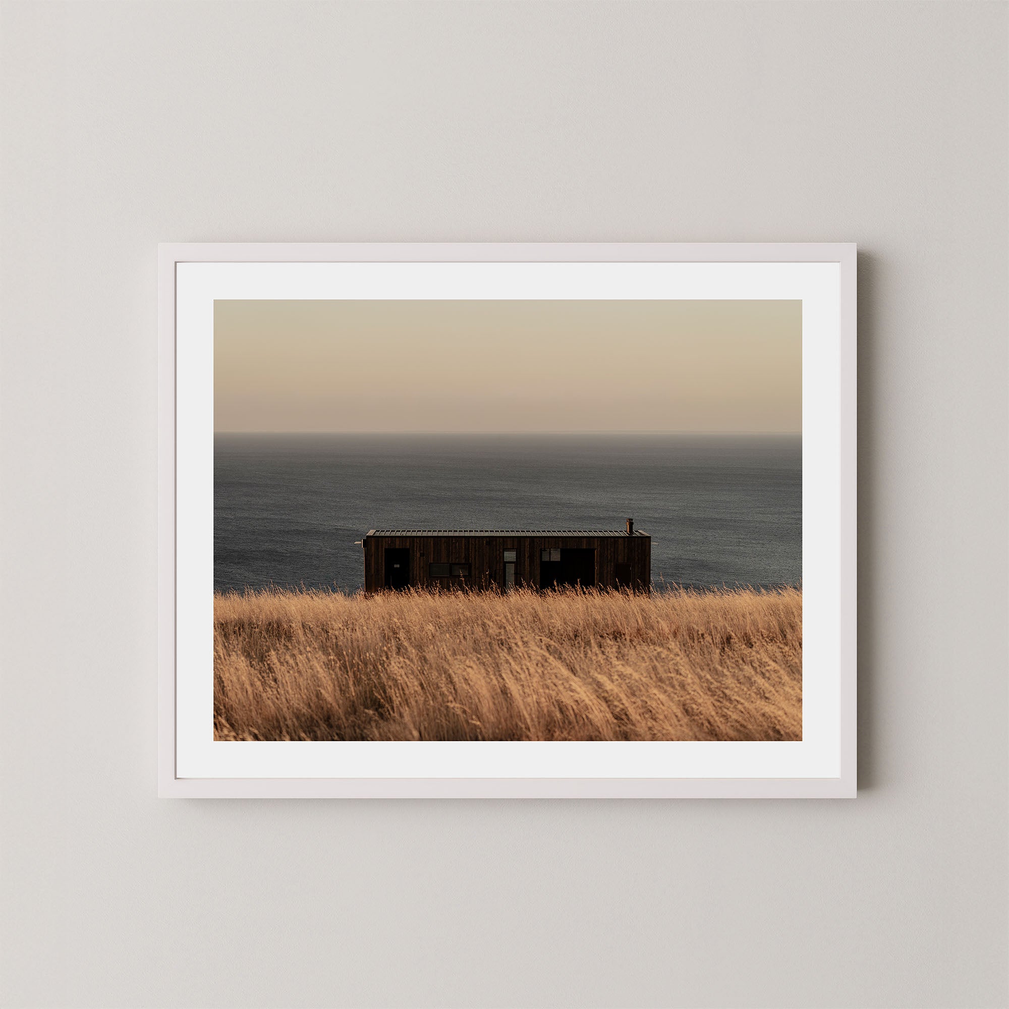 Haven art print of a serene coastal scene with a small building and ocean on Kangaroo Island, Australia, displayed on a wall in a white frame.
