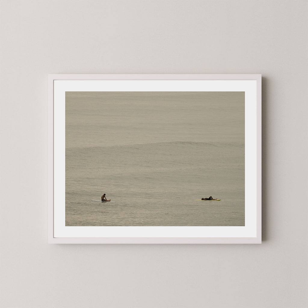 Ocean Therapy art print of two surfers on a calm ocean at Byron Bay, Australia, displayed on a wall in white frame.