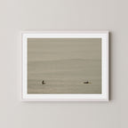 Ocean Therapy art print of two surfers on a calm ocean at Byron Bay, Australia, displayed on a wall in white frame.