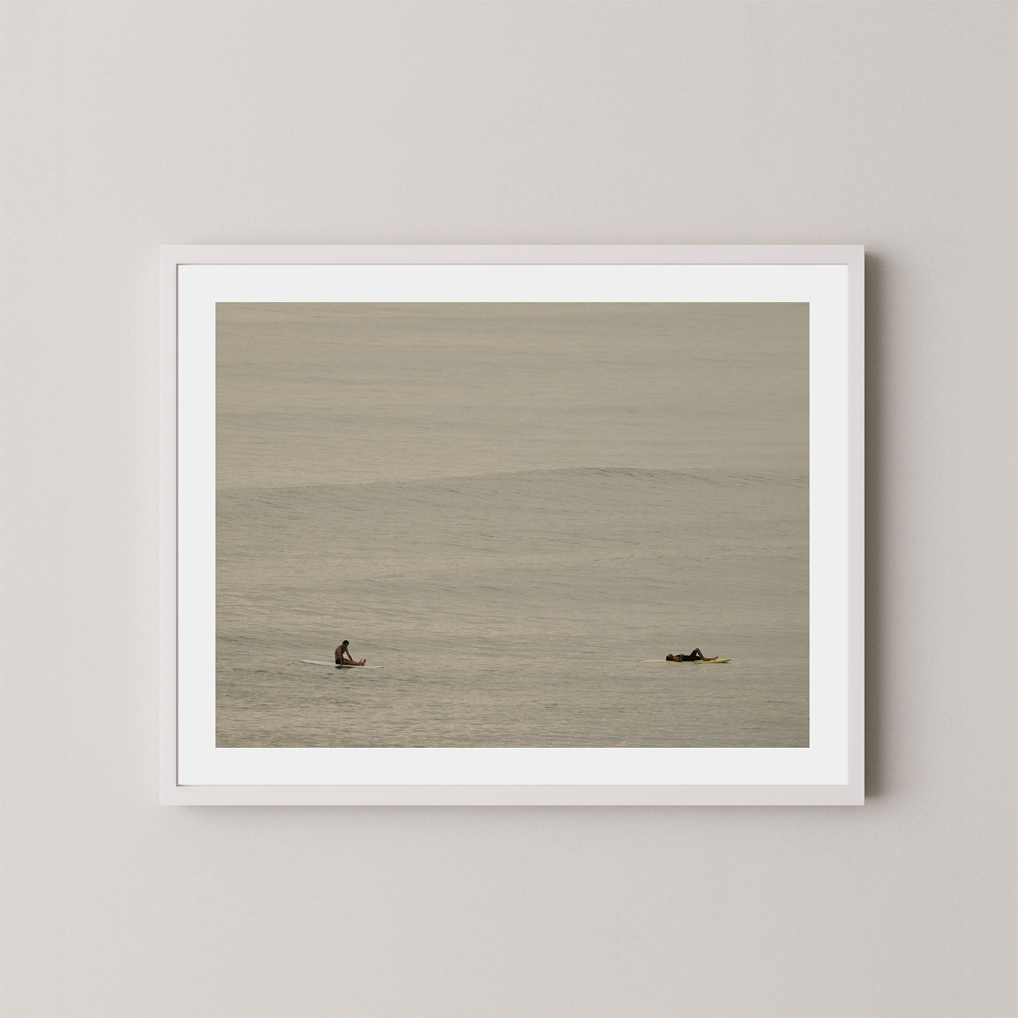 Ocean Therapy art print of two surfers on a calm ocean at Byron Bay, Australia, displayed on a wall in white frame.