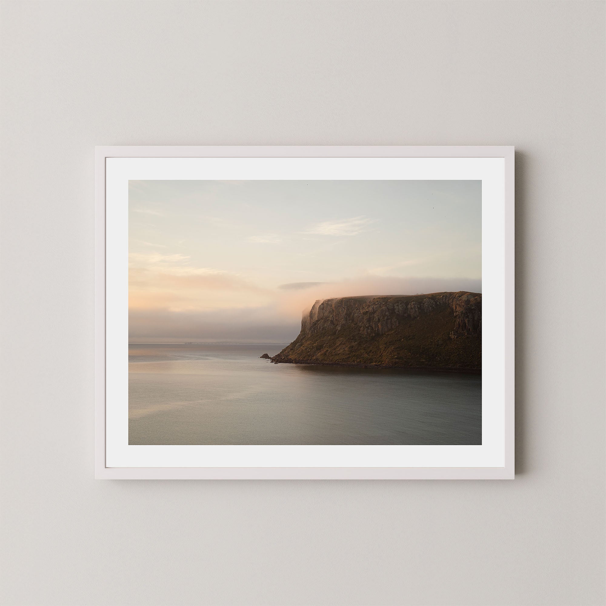 Silent Coast art print of a coastal cliff and sunrise in Stanley, Tasmania, displayed on a white wall in a white frame.