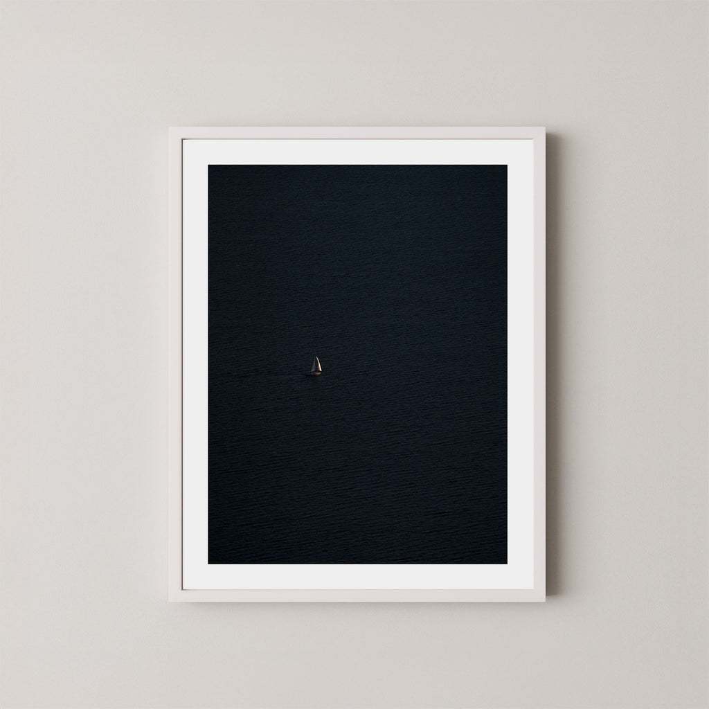 Voyage art print featuring a single sailing boat on the ocean, displayed on a wall in a white frame.