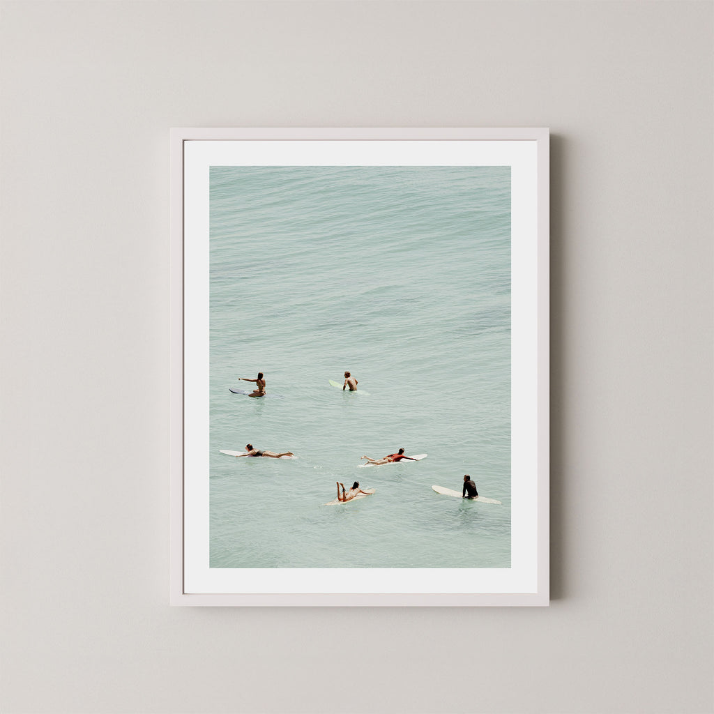 Fine photography artwork of people on surfboards in the water, displayed in a white frame. 