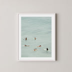 Fine photography artwork of people on surfboards in the water, displayed in a white frame. 